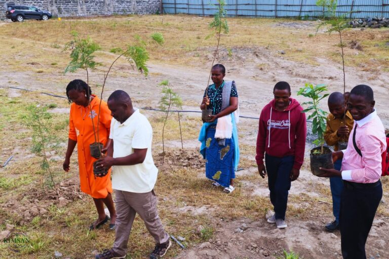 KIMSAN participants carrying young trees across a planted site during a tree-planting activity.