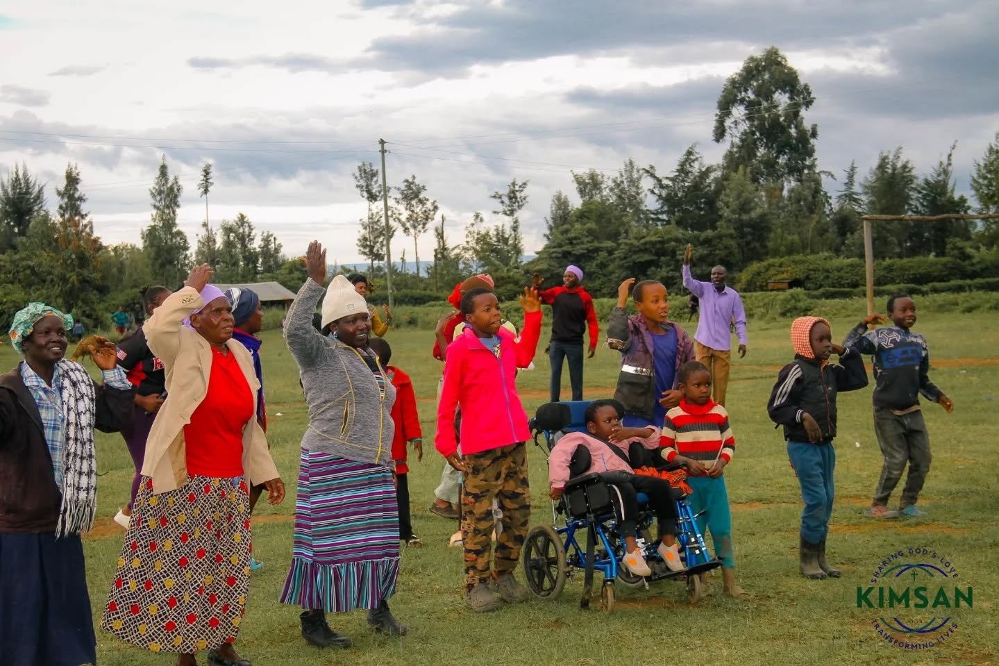 Community members, including children and a wheelchair user, participating during an outdoor KIMSAN Easter mission at San Marco, Salgaa.