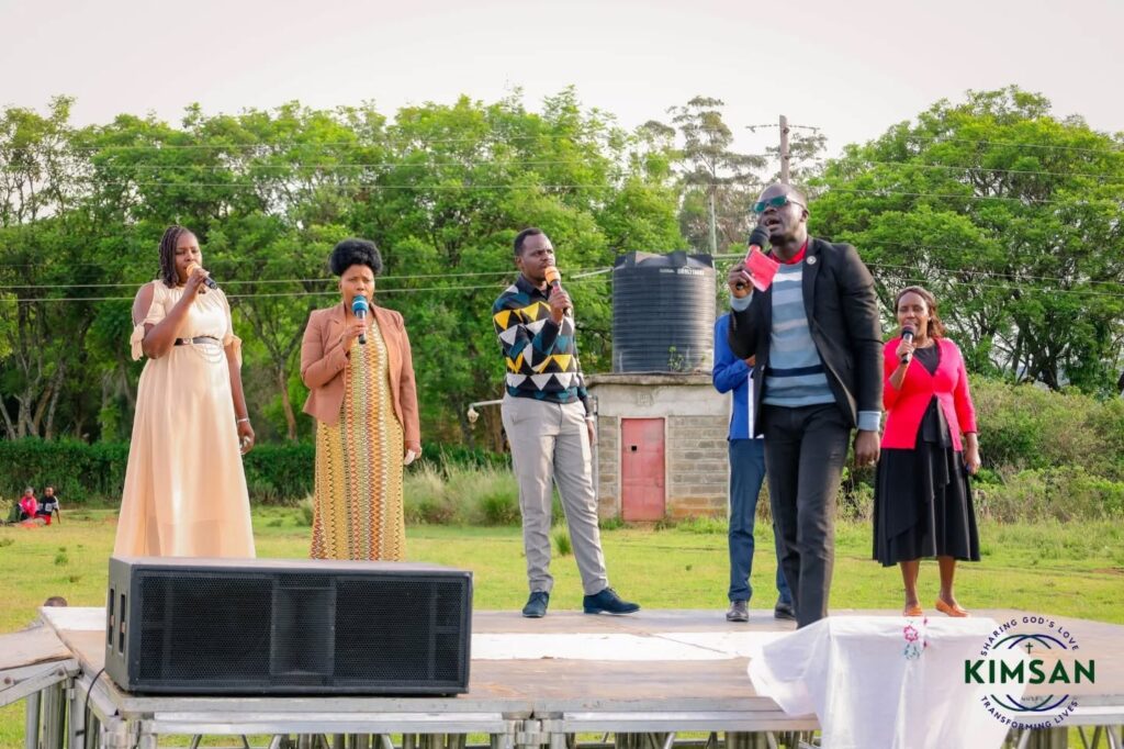 Five KIMSAN ministry participants speaking and singing on an outdoor stage during the Easter Mission at San Marco, Salgaa.